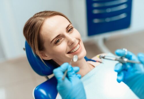 uśmiechnięta kobieta u stomatologa na niebieskim fotelu